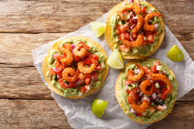 Crispy tostadas topped with guacamole, spiced shrimp, and fresh salsa closeup on the table. Horizontal top view